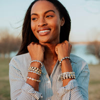 Woman in striped shirt wearing stack of Benedictine Blessing Bracelets in a variety of colors