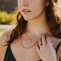 Close up of young women in black dress wearing a gold tone Blessings & Grace Nekclace