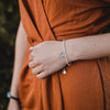Woman in orange dress wearing a silver tone Rays of Light Miraculous Light Bracelet