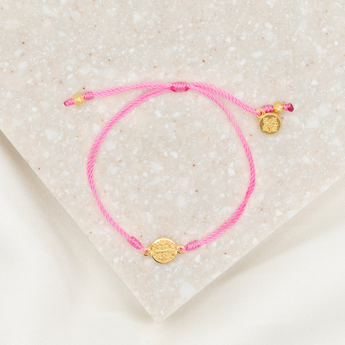 gold-tone St. Benedict medal on pink bracelet cording with a slipknot closure