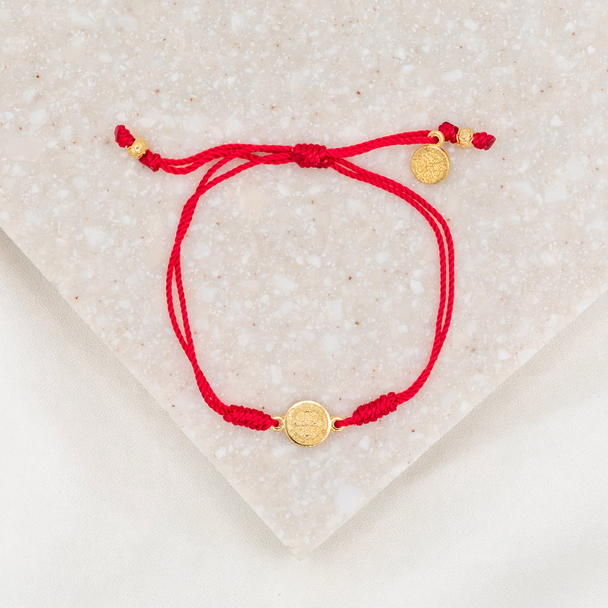 gold-tone St. Benedict medal on red bracelet cording with a slipknot closure