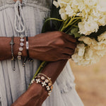close up of woman wearing a bracelet stack on both arms including the silver and black slip know Hope Words of Wisdom Bracelet