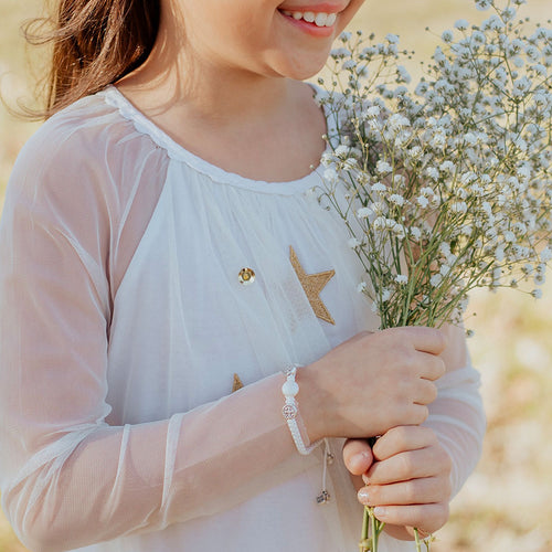 First Holy Communion Blessing Bracelet Crystal Pearl and two Benedictine Medals on young person in field holding bouquet of baby's breath flowers