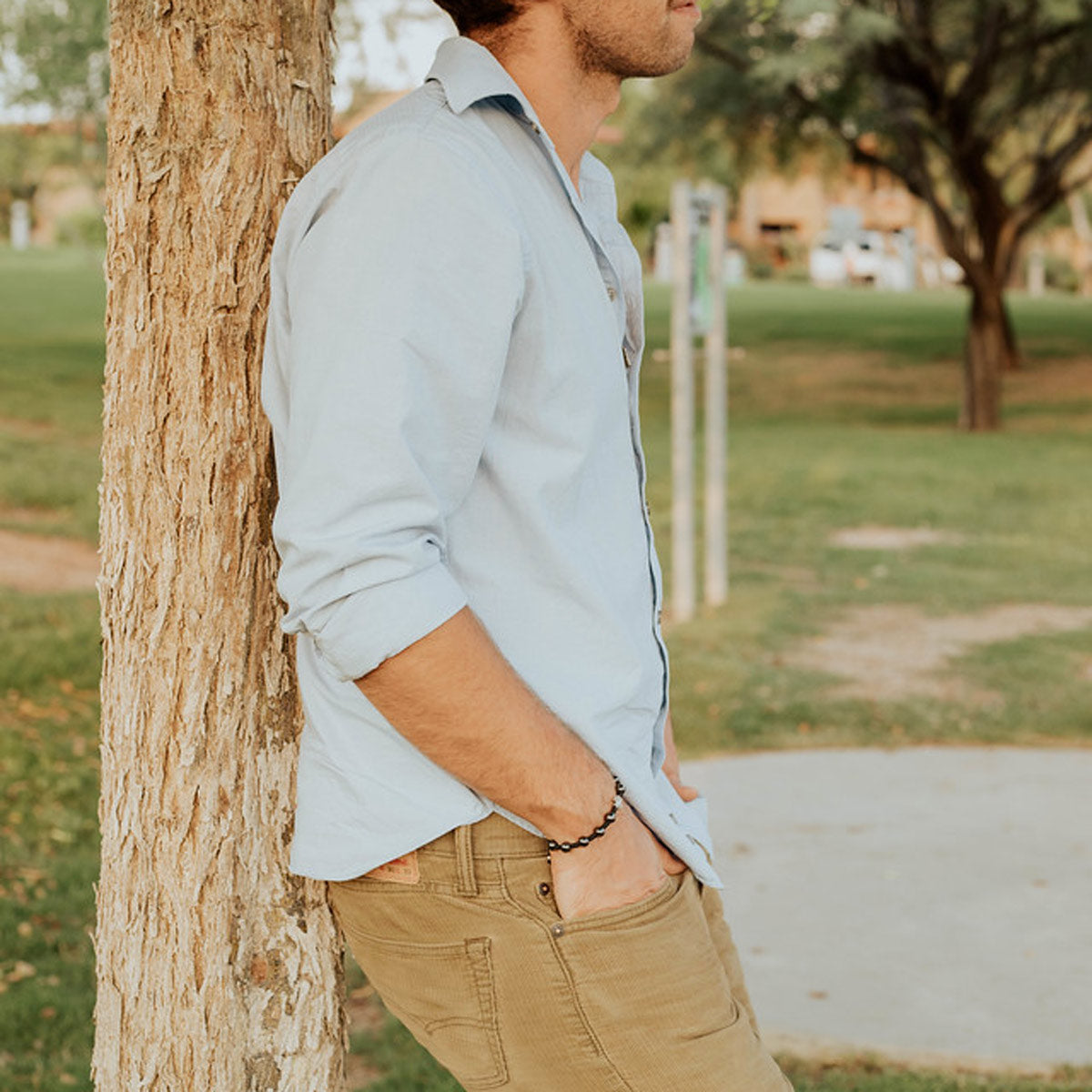 black hemitite and woven cording with cross medal worn on man leaning on tree