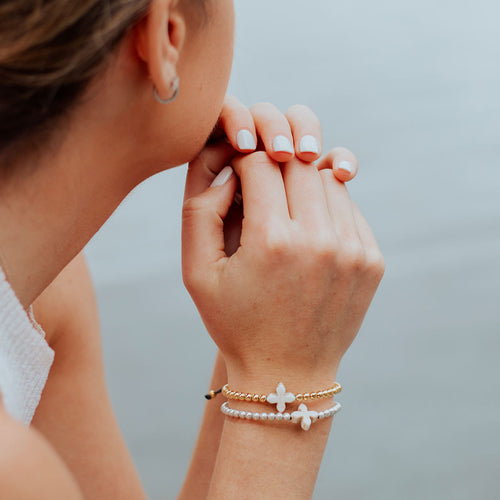 Woman with hands folded looking to the left wearing a gold and silver version of the beaded howlite cross  Living Lent Bracelets