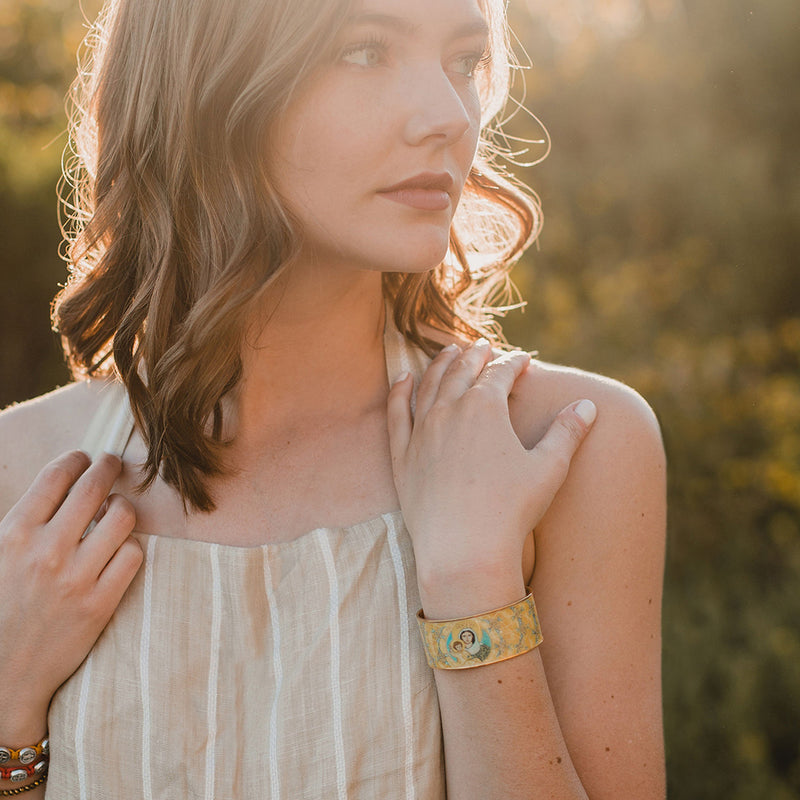 Young woman wearing a Magnificat Sacred Icon Cuff in a field with the sun behind her