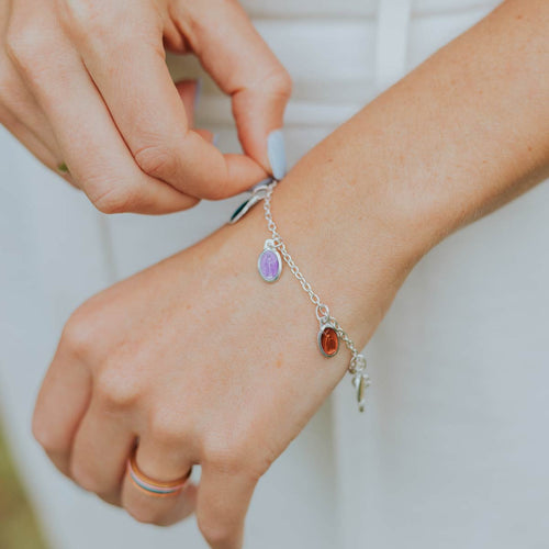 close up of woman's wrist wearing colorful enamel charm bracelet with petite Miraculous Medals