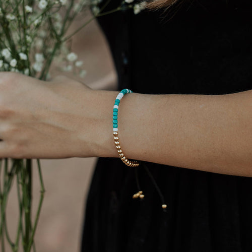 Woman's arm shown wearing a gold tone Beloved Morse Code Blessing Bracelet and holding baby's breathe flowers