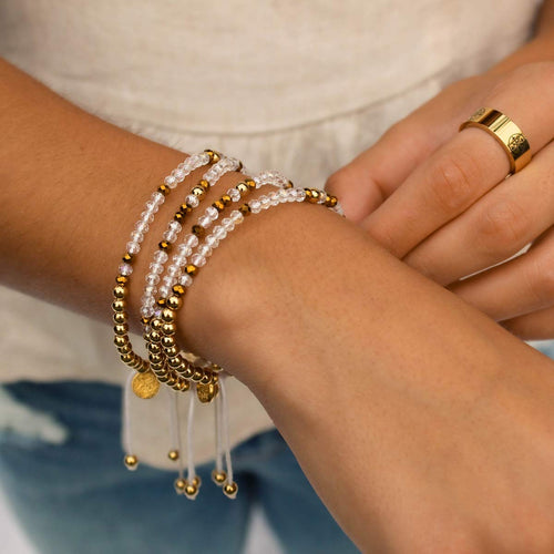 extreme close up of a person's wrist wearing a stack of gold tone and crystal bead morse code sliding know bracelets