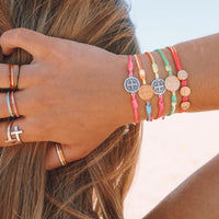 Girl with her hand in her hair wearing a stack of Rainbow and Benedictine Blessing Bracelets
