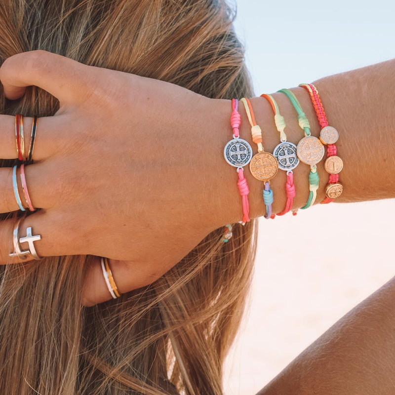 Girl with her hand in her hair wearing a stack of Rainbow and Benedictine Blessing Bracelets