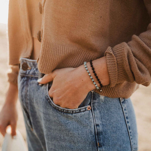 close up of person in brown sweater and jeans wearing amazonite and black agate hand knotted day by day bracelets